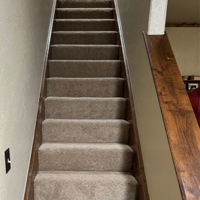 Carpeted staircase with gray steps leading upward, flanked by light-colored walls and wooden trim along the side.
